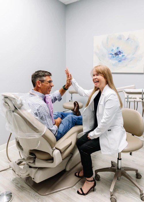 Dr. Phuong-Uyen Le in a white lab coat giving a high five to a male patient sitting in a dental chair.